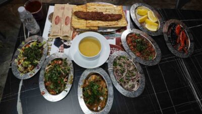 Tescilli Adana kebabı ve yanında servis edilen bol yeşillikli salatalar,